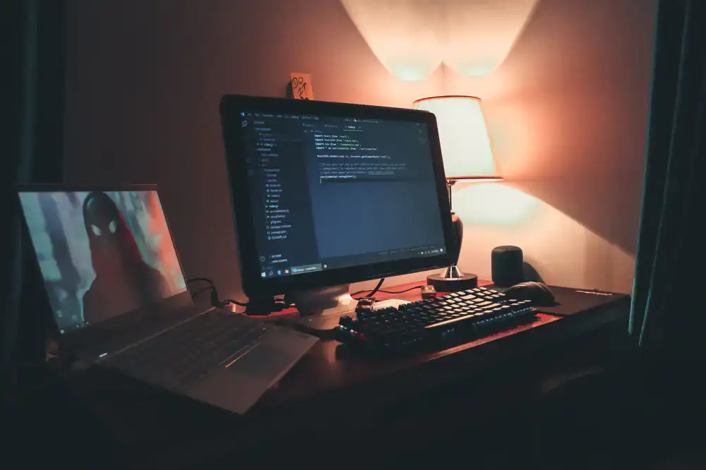 Two programmers collaborating at a dual-monitor setup, reviewing game code